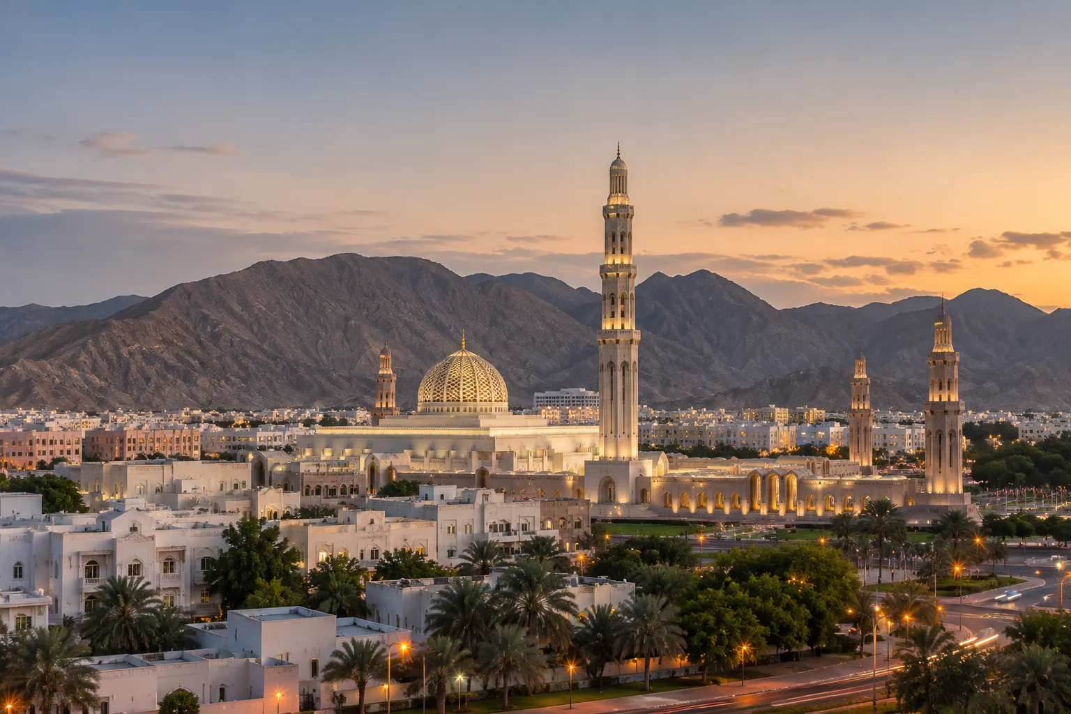 Muscat at dusk — the Grand Mosque's dome and minaret lit warm against the Hajar mountains, white low-rise city all around.